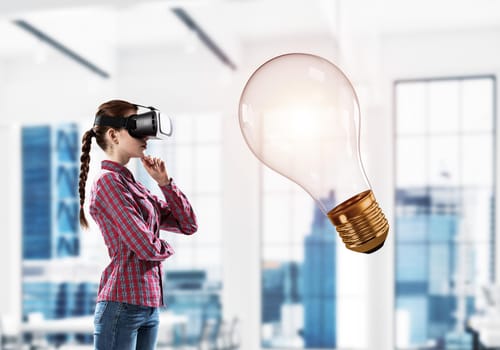 Young woman in virtual reality helmet and glass light bulb. Mixed media