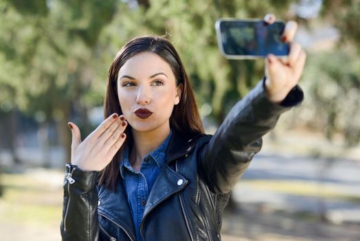 Portrait of a beautiful young woman selfie in the park with a smart phone. Girl blowing a kiss.