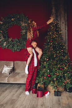 Full length of Caucasian blonde girl sitting on man’s shoulders and decorating xmas tree. Xmas time.