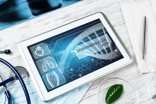 Human genetic research in medical laboratory. Tablet computer with DNA helix structure on screen. Stethoscope, x-ray image and cardiogram on wooden desk. Medical diagnostics and patient genome testing