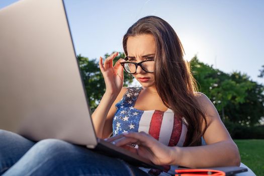 Pretty young woman sitting on bean bag use laptop while resting on grass in park on the sun. Success small business, modern lifestyle, information technology, or online shopping concept