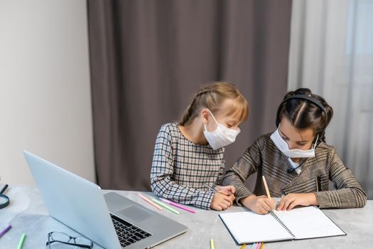 Distance Learning. School Girls At Laptop Wearing Mask Studying Online Sitting at the table at home