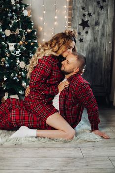 Couple in red checked pyjamas hugging on the floor. Girl kissing her boyfriend’s forehead.