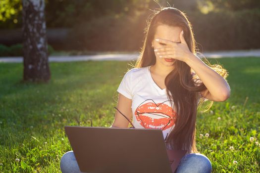 Young woman using computer on green grasses in the park. Education learning or freelance working outdoor or relaxation concept idea background. Modern lifestyle, information technology or online shopping concept