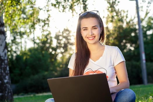 Young woman using computer on green grasses in the park. Education learning or freelance working outdoor or relaxation concept idea background. Modern lifestyle, information technology or online shopping concept