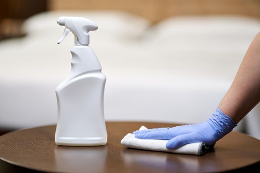 Close up of chambermaid cleaning and polishing wooden table with a spray detergent in hotel room. Housekeeping and hygiene concept