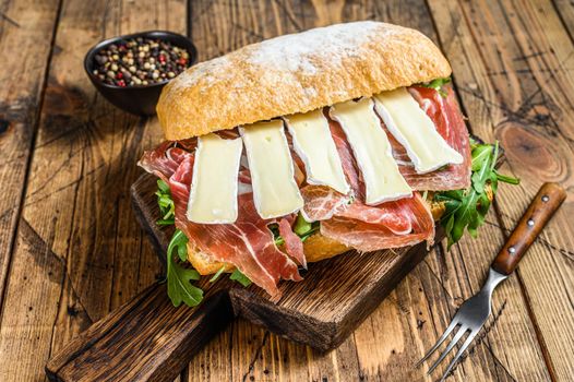 Parma Ham Sandwich on ciabatta bread with arugula and camembert brie cheese. wooden background. Top view.