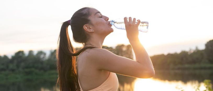 Beautiful fitness athlete woman drinking water after workout exercising on sunset evening summer in beach outdoor portrait.