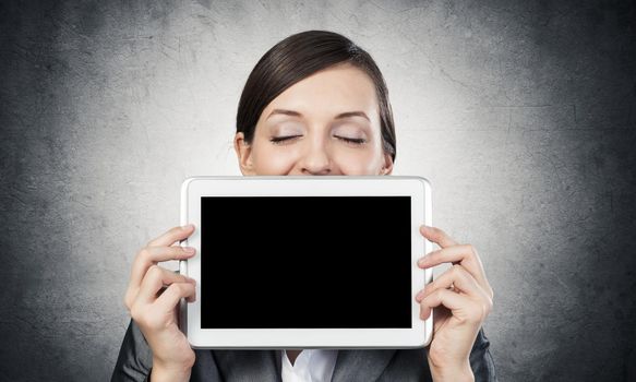 Businesswoman holding tablet computer with blank screen. Beautiful woman with closed eyes showing tablet PC near her face. Corporate businessperson on grey wall background. Digital technology