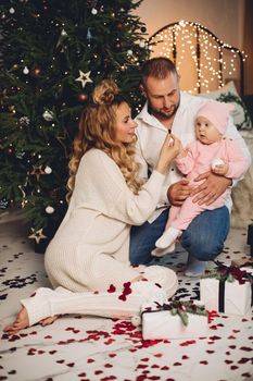 Photo of loving parents playing with confetti with baby daughter on father’s thigh. Christmas.