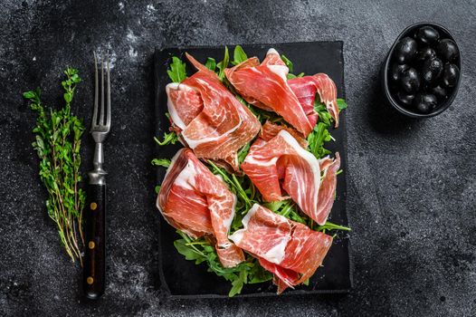 Sliced Jamon serrano pork ham meat on a marble board. Black background. Top view.