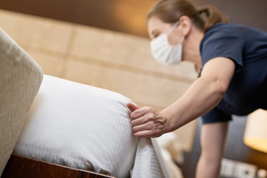 Low angle view of mousemaid tucking the sheet on the bed in the hotel room. Hotel service concept