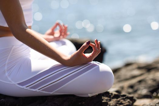 Young woman doing yoga in the beach. Female wearing sport clothes in lotus figure with defocused background.