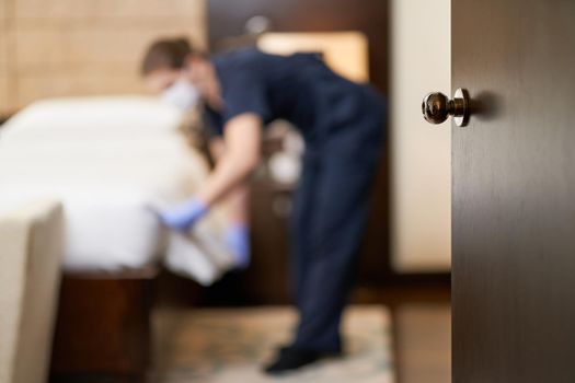Wooden door to hotel room with maid during cleaning in the background. Hotel service concept