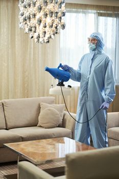 Worker in blue chemical protection suit doing disinfection and spraying of room. Coronavirus and quarantine concept