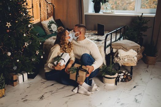 Pretty caucasian girl and her boyfriend in the bedroom in christmas atmosphere with medical masks