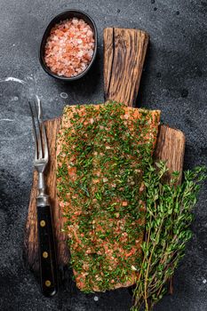 Gravlax cured salmon with dill and salt on wooden board. Black background. Top view.