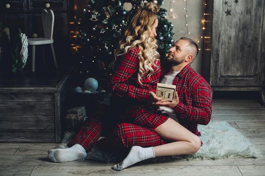 Beautiful couple in red checked pajamas holding wooden calendar with 31st date. New Year’s Eve.