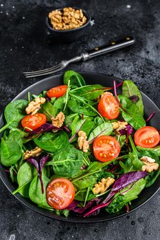 Vegetarian salad with mix leaves mangold, swiss chard, spinach, arugula and nuts in a salad bowl. Black background. Top view.