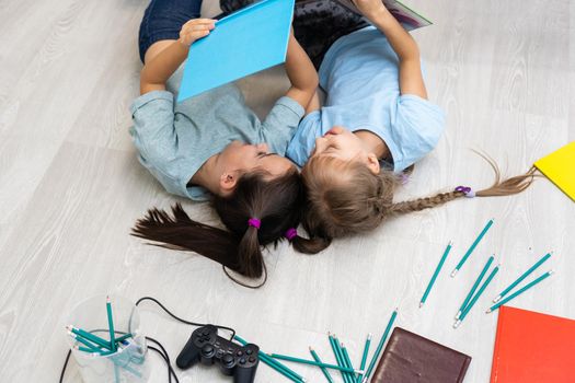 family, leisure and childhood concept - happy sisters lying on floor and drawing and doing homework at home