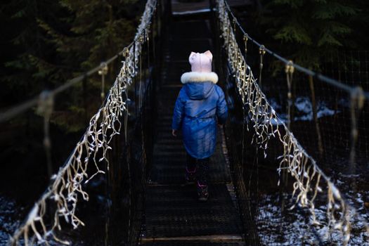 little girl on suspension bridge in the evening among Christmas lights.