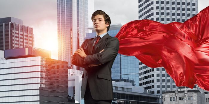 Young confident businessman wearing red cape against modern city background
