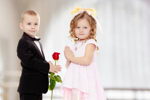 Little boy in black suit with bow tie gives a big red rose charming little girl.