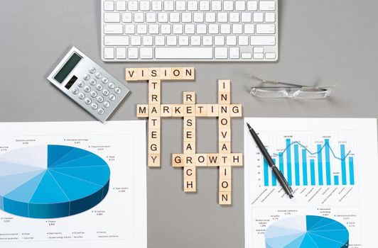 Business motivation concept with words from cubes. Still life of office workplace with crossword. Flat lay grey surface with computer keyboard and calculator. Strategy planning and business analytics