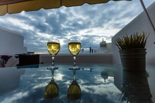 Two glasses with cold white wine served outside on terrace with pink tropical flowers, luxury resort with sea view, romantic vacation, honeymoon.