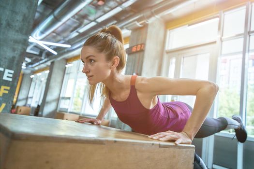 Young athletic woman in sportswear doing push ups on wooden crossfit jump box at gym. Sportive people, healthy lifestyle and workout concept