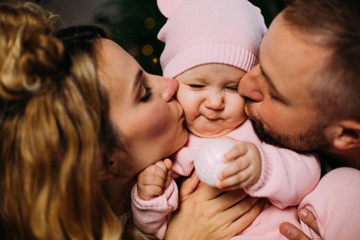 Close up of happy dad and mom kissing their cute baby. Parenthood and family concept