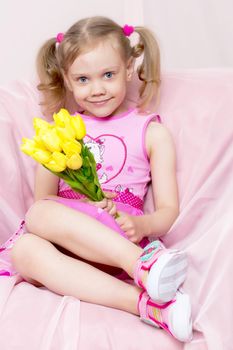 Happy little girl with a bouquet of flowers sitting on the couch. The concept of a holiday, spring mood, birthday and family happiness.
