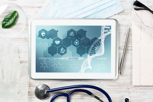 Human genetic research in modern medical laboratory. Tablet computer with DNA helix structure on screen. Stethoscope and cardiogram on wooden desk. Medical diagnostics and patient genome testing.