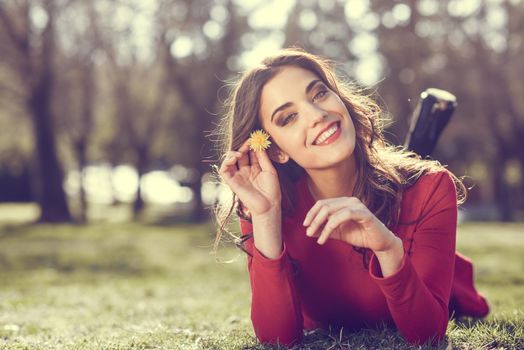 Portrait of young woman rest in the park with a dandelion in her hair, lying on the grass