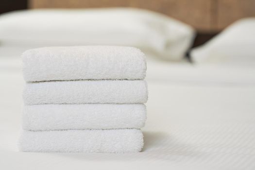 Close up of four white towels on bed in hotel room for customer. Copy space. Hotel service concept