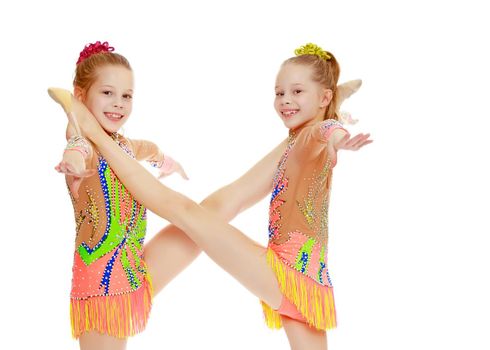 Two adorable little twin girls, gymnastics in the sports school. Girls beautiful gymnastic leotards. They do the splits.Isolated on white background.