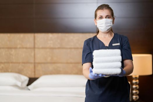 Waist up of maid keeping bunch of clean towels in the room. Copy space. Hotel service concept