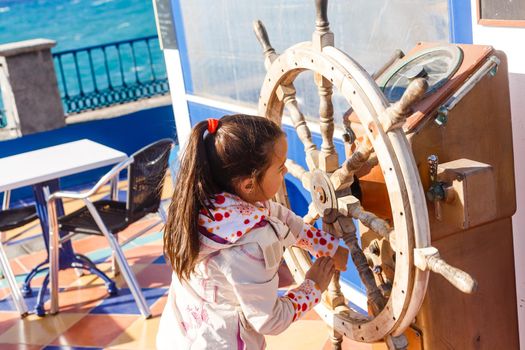 cute little girl holding a ship steering wheel in an amusement park