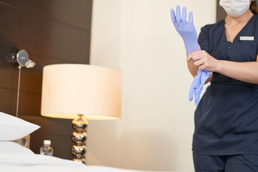 Cropped photo of maid in uniform putting on protective gloves before cleaning. Hotel service concept