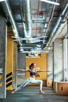 Life balance. Full length of a young caucasian woman in sportswear practicing yoga at gym, vertical shot. Sport, wellness and healthy lifestyle