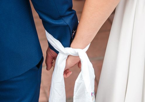 The bound hands of the bride and groom holding together tightly close up.