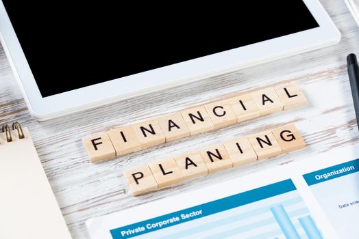 Financial planning concept with letters on cubes. Still life of office workplace. Flat lay vintage wooden desk with tablet computer and analytic report. Company development and consulting analysis.