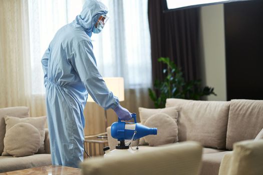 Worker in a protective suit and mask while disinfecting the room from viruses. Coronavirus and quarantine concept