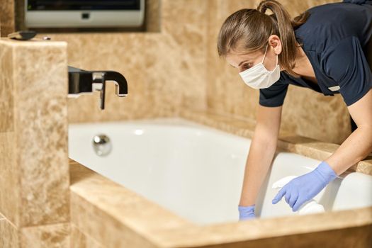 Maid in protective gloves cleaning bathroom in a hotel room. Hotel service concept