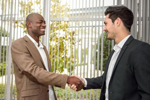 Black businessman shaking hands with a caucasian one wearing suit in a office. Two men smiling