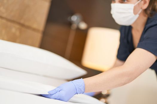 Close up of chambermaid setting white bed blanket in hotel room. Hotel service concept. Copy space