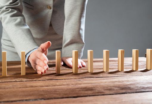 Businesswoman interrupting domino effect by stop falling wooden dominoes. Operative business solution, strategy and successful intervention. Business assistance, protection and prevention of crisis