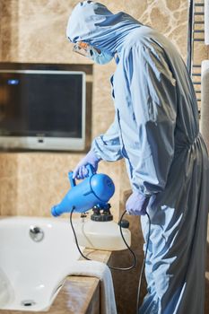 Side view of of worker in biohazard suit using disinfectant in hotel bathroom. Coronavirus and quarantine concept