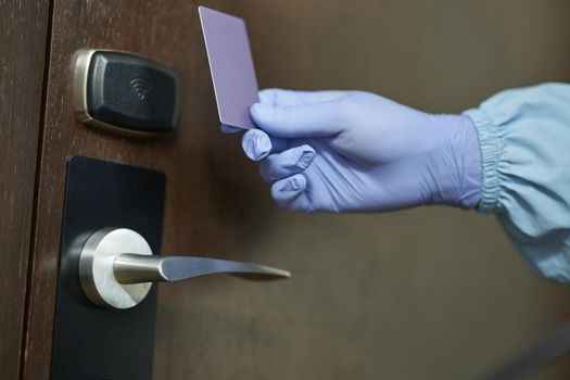 Close up of worker in blue suit and protective gloves holding card in front of the door to the room. Coronavirus and quarantine concept