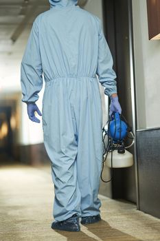 Back view of male specialist in blue suit with disinfectant going to sanitize room in hotel. Coronavirus and quarantine concept